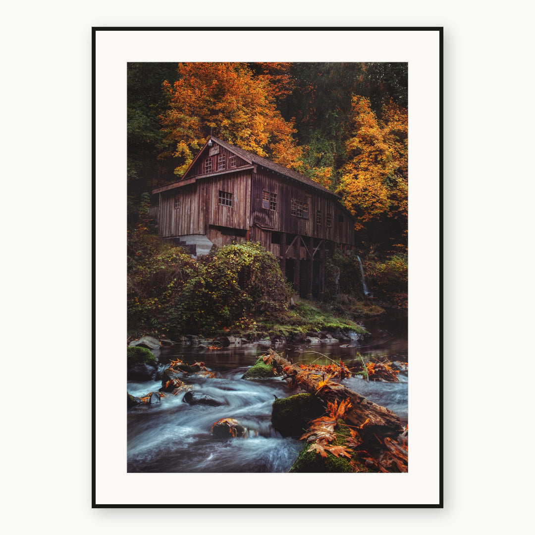 Wooden grist mill beside a rocky creek and orange autumn foliage, shown with a white mat and thin black frame.